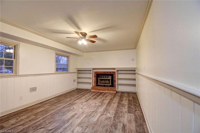 unfurnished living room featuring a brick fireplace, ceiling fan, wood-type flooring, and ornamental molding