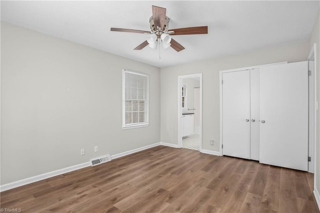 unfurnished bedroom featuring a closet, visible vents, ensuite bathroom, wood finished floors, and baseboards