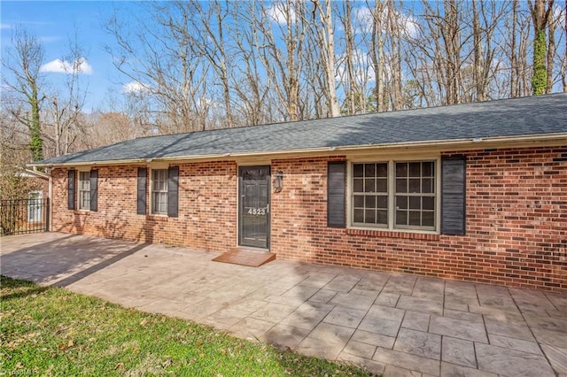 ranch-style home with brick siding, roof with shingles, and a patio