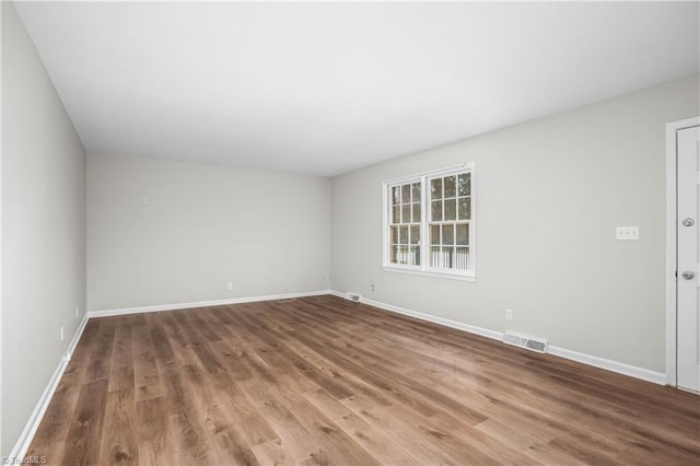 spare room featuring baseboards, visible vents, and wood finished floors