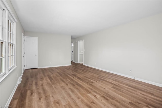 empty room featuring baseboards, a wealth of natural light, and light wood-style floors