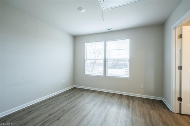 unfurnished room with baseboards, attic access, visible vents, and wood finished floors