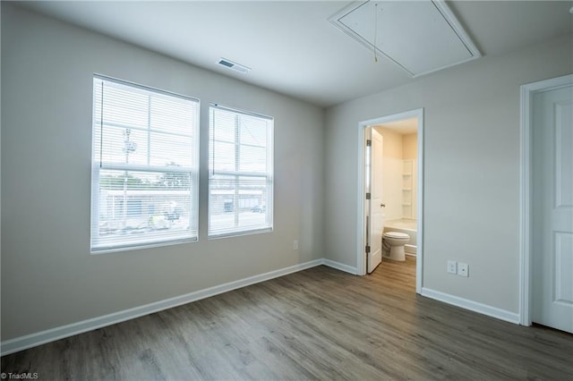 unfurnished bedroom featuring connected bathroom, wood finished floors, visible vents, baseboards, and attic access