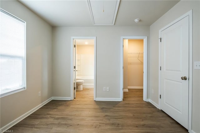 unfurnished bedroom with attic access, a walk in closet, baseboards, and wood finished floors