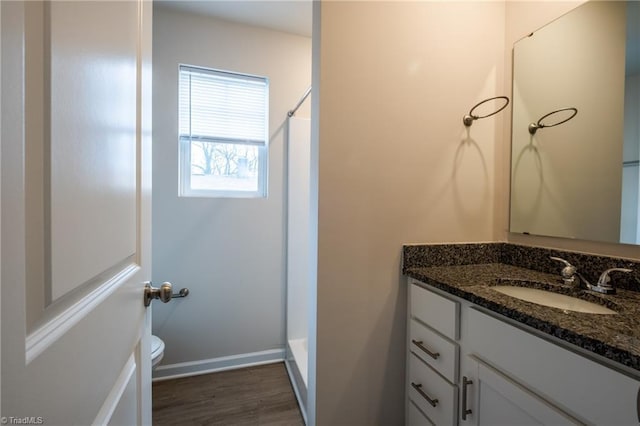 bathroom with baseboards, toilet, wood finished floors, walk in shower, and vanity