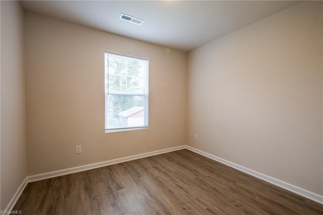 empty room featuring dark wood-type flooring, visible vents, and baseboards