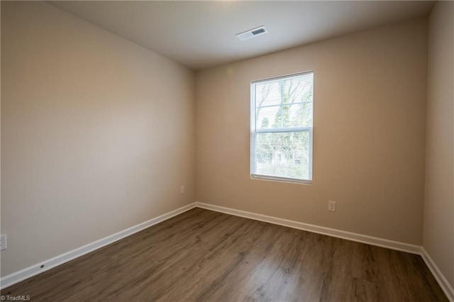 spare room with dark wood-style floors, visible vents, and baseboards