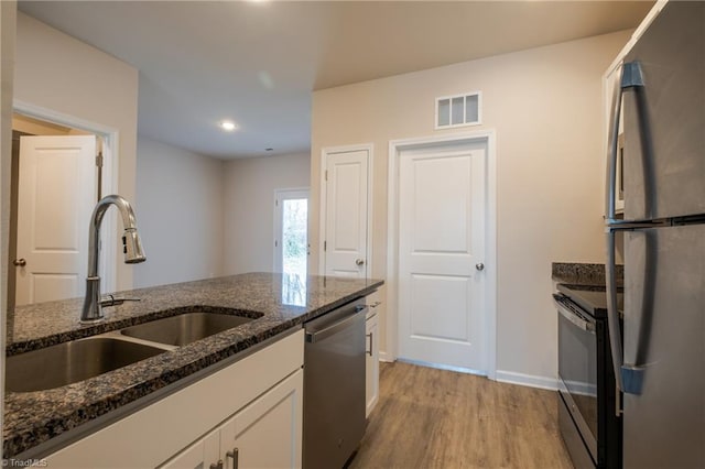 kitchen featuring stainless steel appliances, visible vents, white cabinets, a sink, and dark stone countertops