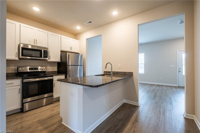 kitchen featuring stainless steel appliances, visible vents, white cabinets, a sink, and dark stone counters