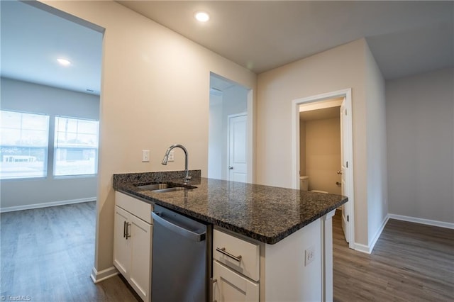 kitchen featuring dark wood-style flooring, stainless steel dishwasher, white cabinetry, a sink, and dark stone countertops