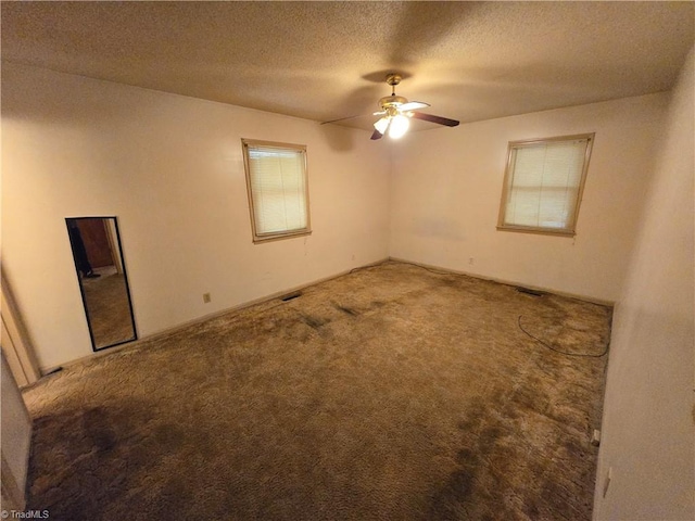 carpeted spare room featuring a textured ceiling, ceiling fan, and a wealth of natural light