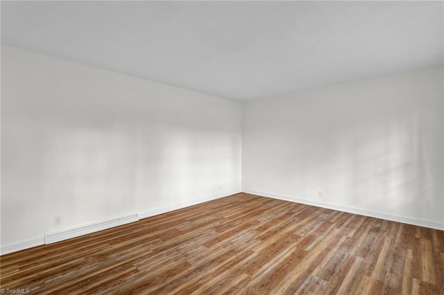 unfurnished room featuring a baseboard heating unit and hardwood / wood-style floors