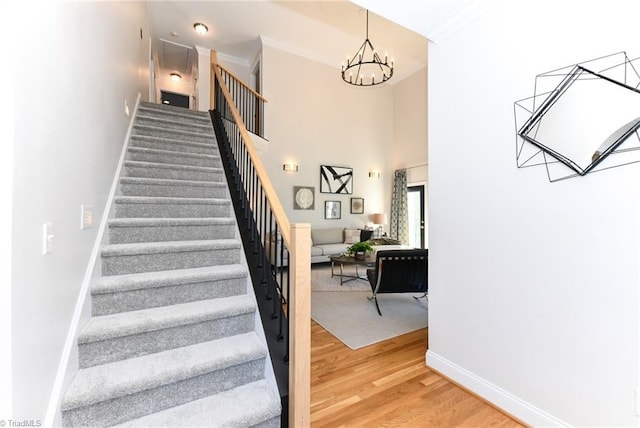 staircase with wood-type flooring, crown molding, and an inviting chandelier