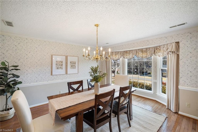 dining space with an inviting chandelier, hardwood / wood-style flooring, ornamental molding, and a textured ceiling