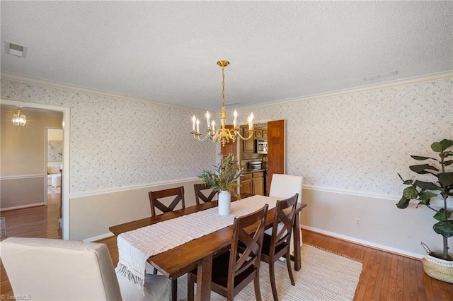 dining room featuring ornamental molding, wood-type flooring, a chandelier, and a textured ceiling