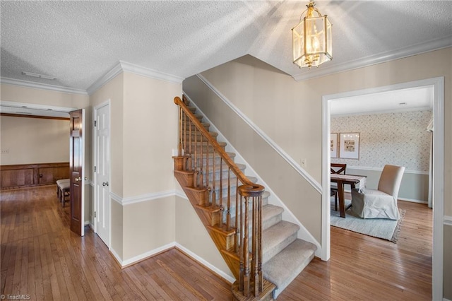 stairs with ornamental molding, hardwood / wood-style floors, and a textured ceiling