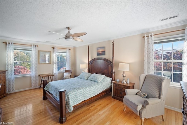 bedroom with ceiling fan, ornamental molding, light hardwood / wood-style floors, and a textured ceiling