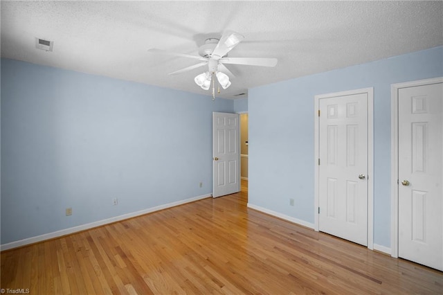 unfurnished bedroom featuring multiple closets, ceiling fan, a textured ceiling, and light hardwood / wood-style floors