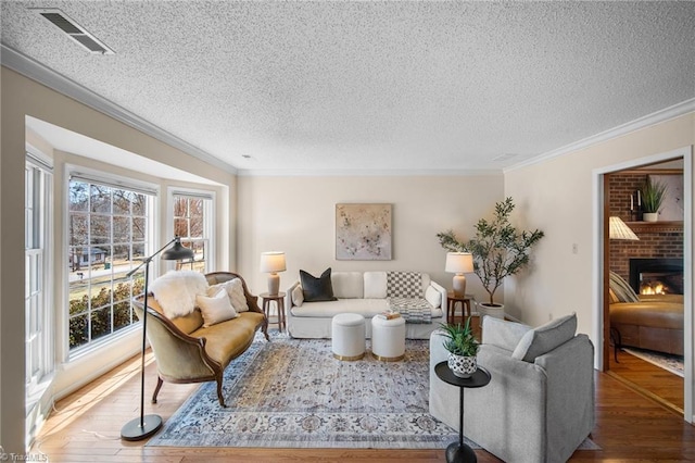 living room featuring ornamental molding, wood-type flooring, a textured ceiling, and a fireplace