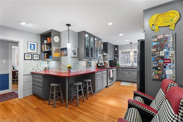 kitchen with backsplash, gray cabinetry, light wood-style flooring, stainless steel appliances, and open shelves