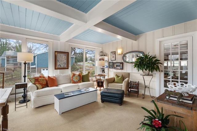 carpeted living room featuring a wealth of natural light, beam ceiling, and a decorative wall