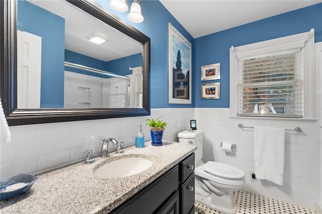 bathroom with tile walls, toilet, wainscoting, a stall shower, and vanity