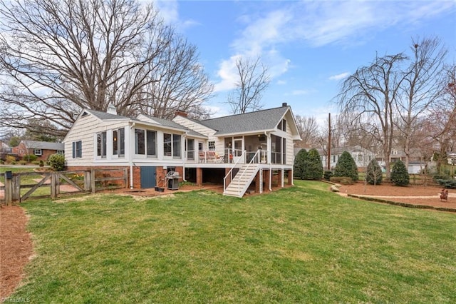 rear view of property featuring fence, stairway, a chimney, a yard, and a sunroom