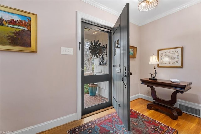 entryway with visible vents, wood finished floors, baseboards, and ornamental molding