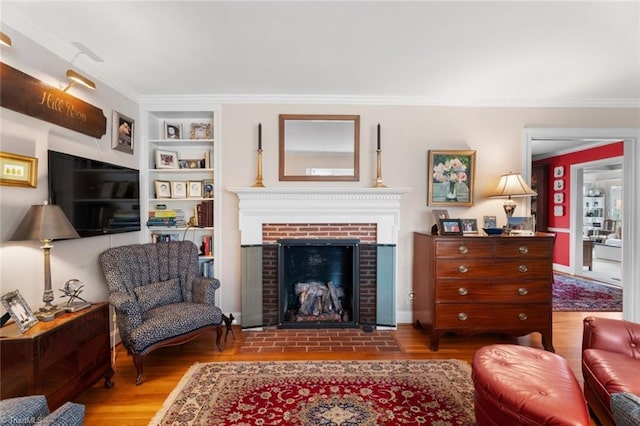 living area featuring crown molding, a brick fireplace, built in features, and wood finished floors