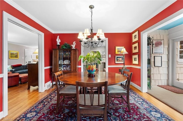 dining area with a chandelier, light wood-style flooring, baseboards, and ornamental molding