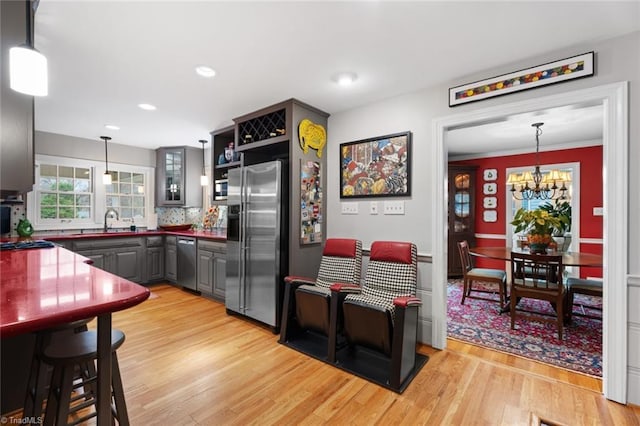 kitchen with gray cabinets, a sink, stainless steel appliances, light wood-style floors, and a notable chandelier