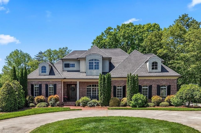 view of front facade featuring curved driveway, a shingled roof, a front lawn, and brick siding