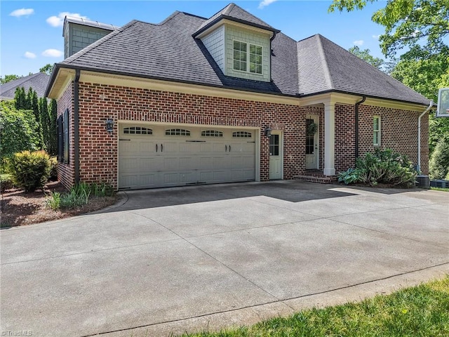 view of front of property with roof with shingles, a garage, central air condition unit, brick siding, and concrete driveway