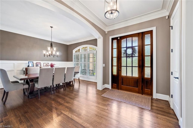 foyer entrance with crown molding, arched walkways, a chandelier, and wood finished floors