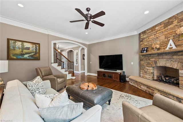 living area with a ceiling fan, crown molding, arched walkways, wood finished floors, and stairs