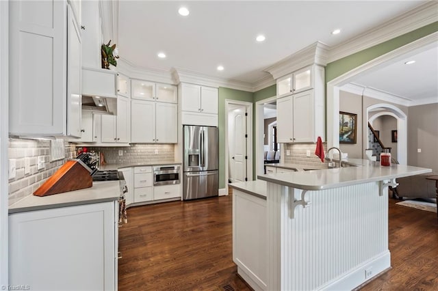 kitchen with a sink, stainless steel appliances, white cabinetry, a peninsula, and tasteful backsplash