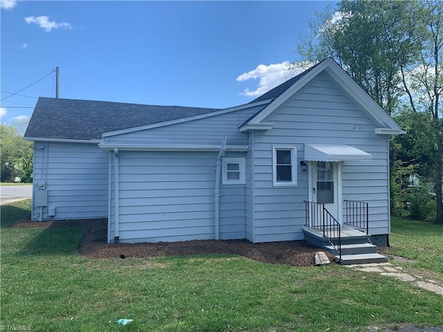 back of house with roof with shingles and a yard