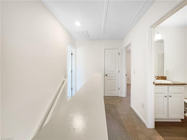 hallway featuring visible vents, an upstairs landing, a sink, carpet, and attic access