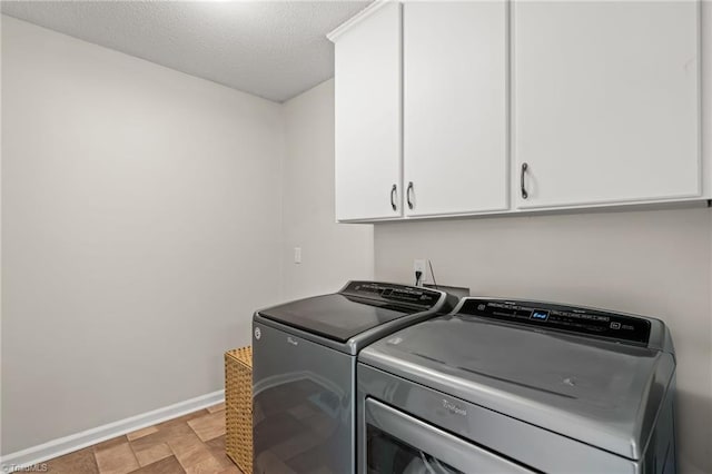 clothes washing area featuring washing machine and clothes dryer, a textured ceiling, and cabinets