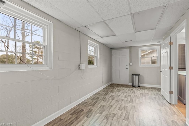 basement with light wood-type flooring, a drop ceiling, and a healthy amount of sunlight