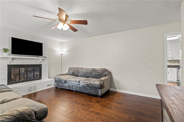 living room with a fireplace, dark wood-type flooring, a textured ceiling, and ceiling fan