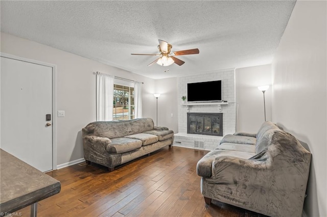 living room with ceiling fan, a textured ceiling, dark hardwood / wood-style floors, and a brick fireplace