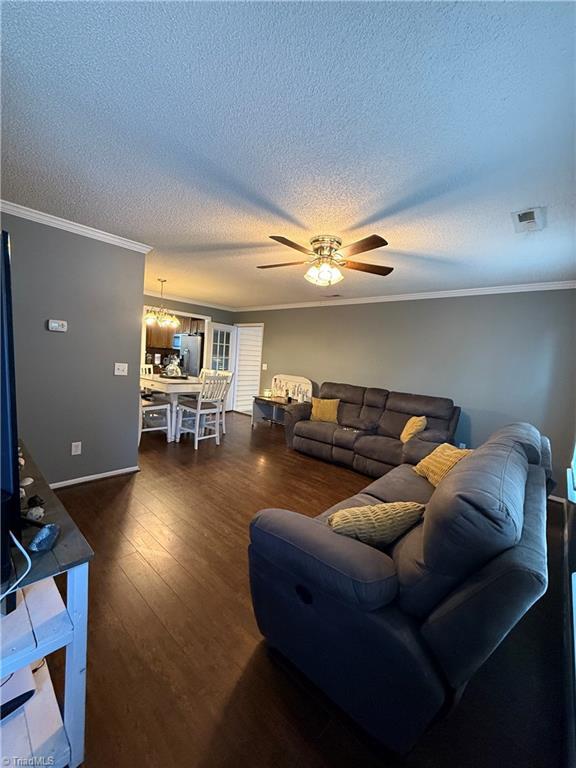 living room featuring dark wood-type flooring, ornamental molding, ceiling fan with notable chandelier, and a textured ceiling