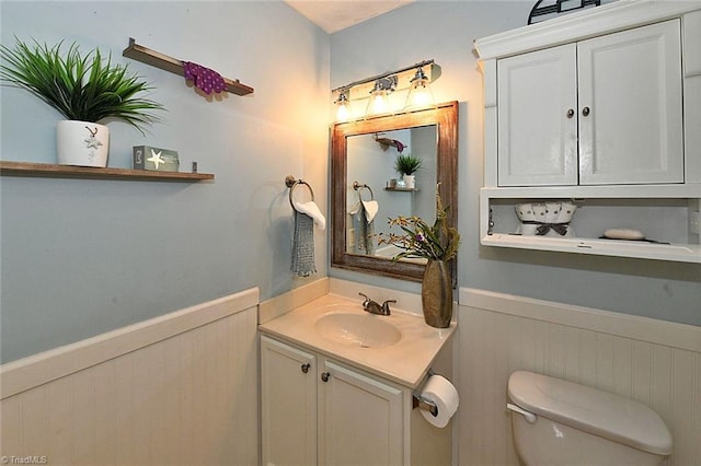 half bath featuring vanity, toilet, and wainscoting