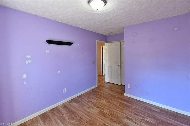 unfurnished bedroom with a textured ceiling, baseboards, and wood finished floors