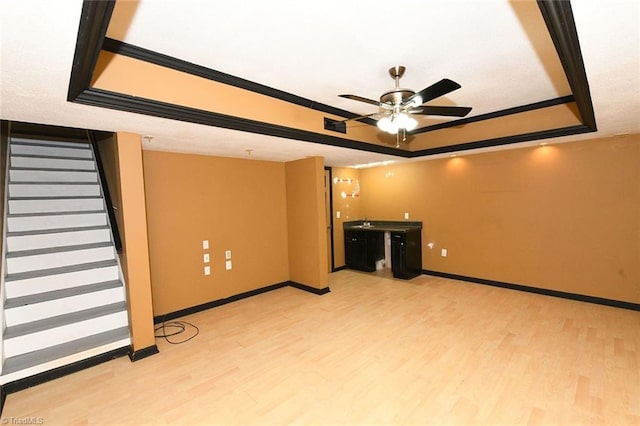 unfurnished living room with stairs, a tray ceiling, light wood-style floors, and ceiling fan