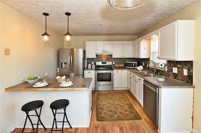 kitchen with a sink, a kitchen breakfast bar, appliances with stainless steel finishes, a peninsula, and light wood finished floors