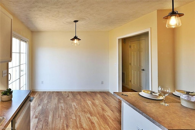 unfurnished dining area featuring baseboards, light wood-style floors, and a textured ceiling