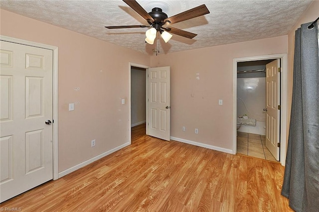 unfurnished bedroom with baseboards, light wood-style floors, ensuite bath, and a textured ceiling