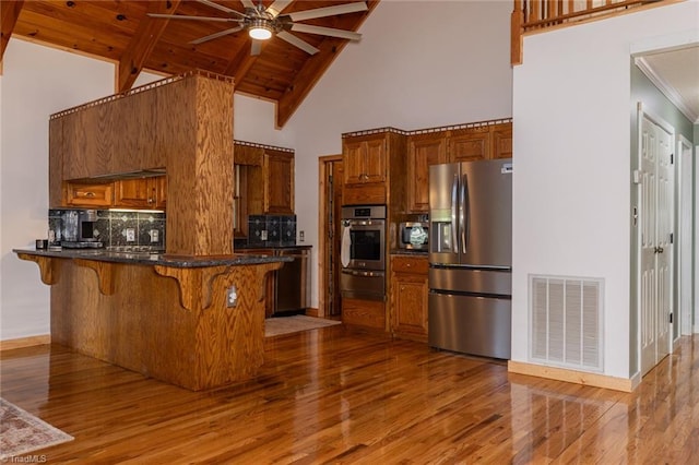 kitchen with hardwood / wood-style flooring, stainless steel appliances, decorative backsplash, high vaulted ceiling, and ceiling fan